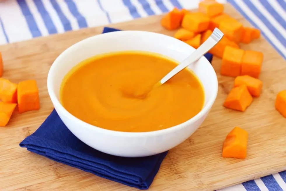 A bowl of ginger butternut squash soup is on a wooden board.