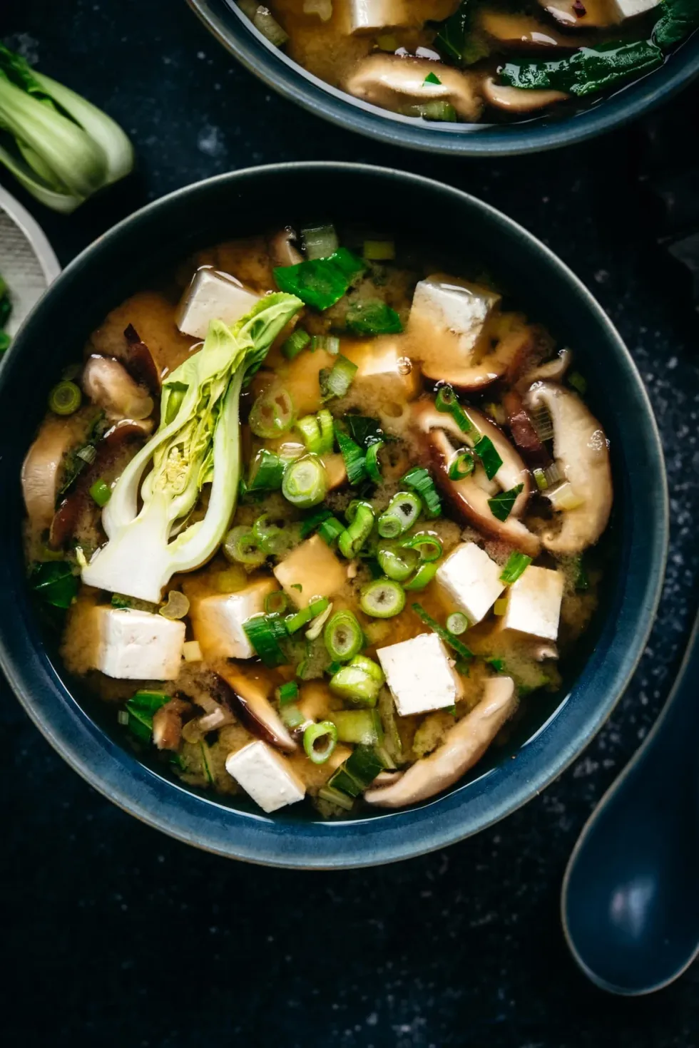 A bowl of miso soup is next to a spoon.