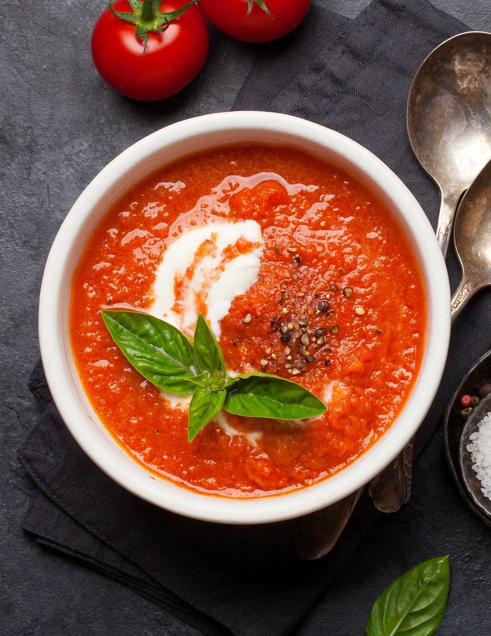 A bowl of tomato soup is on a black surface.