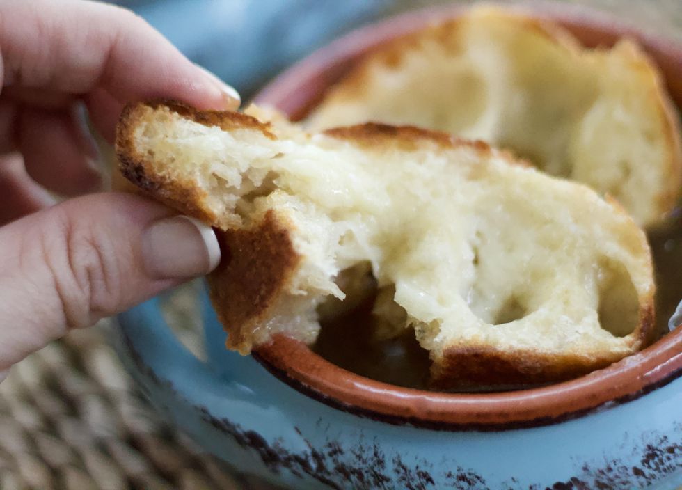 A slice of baguette in a bowl of Slow Cooker French Onion Soup