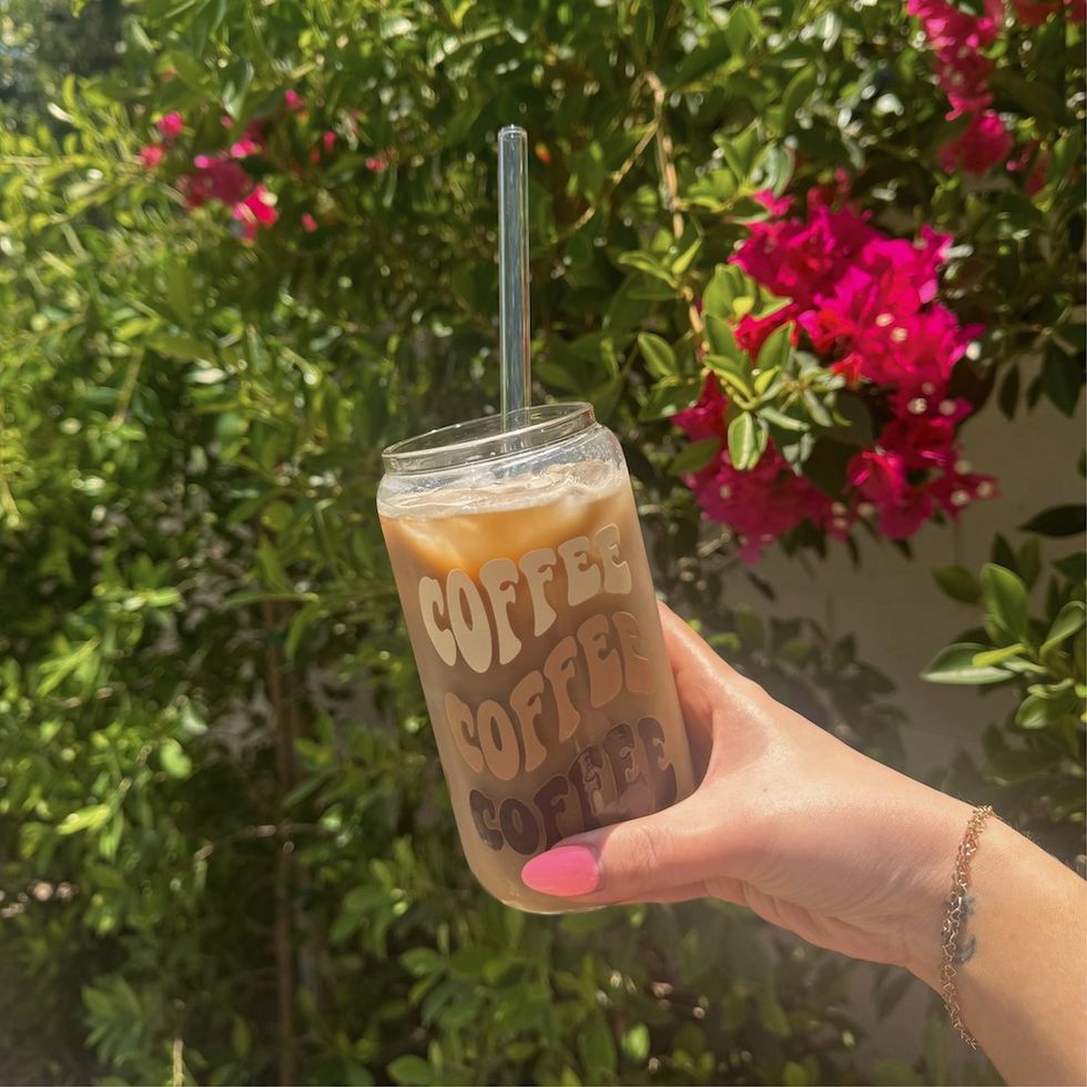 a woman holding an iced coffee in front of some flowers