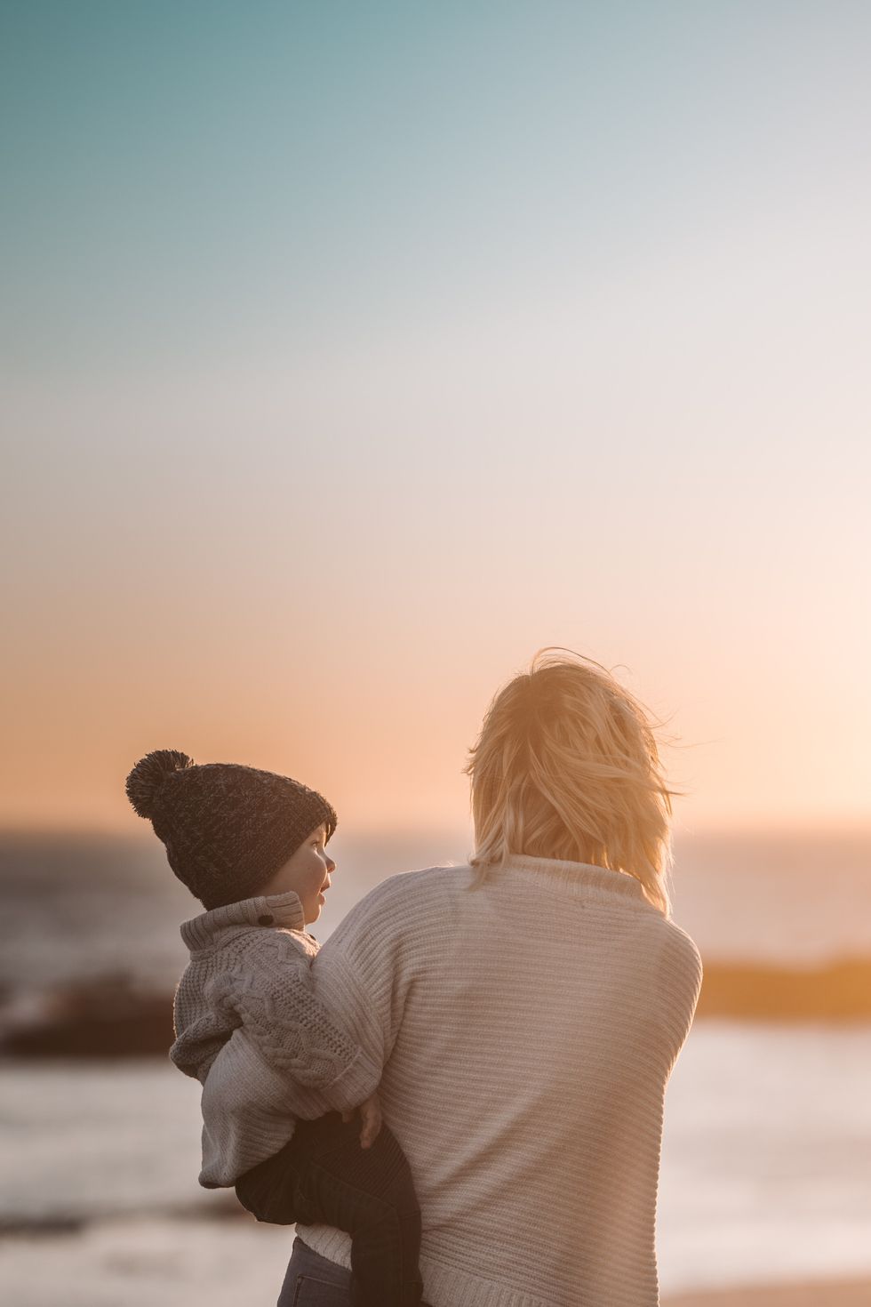 backside view of a woman carrying a child by the ocean