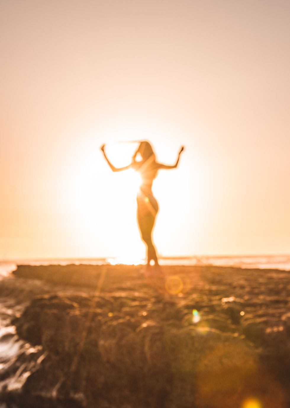 blurred, dreamy image of a person standing by the seaside with their arms up