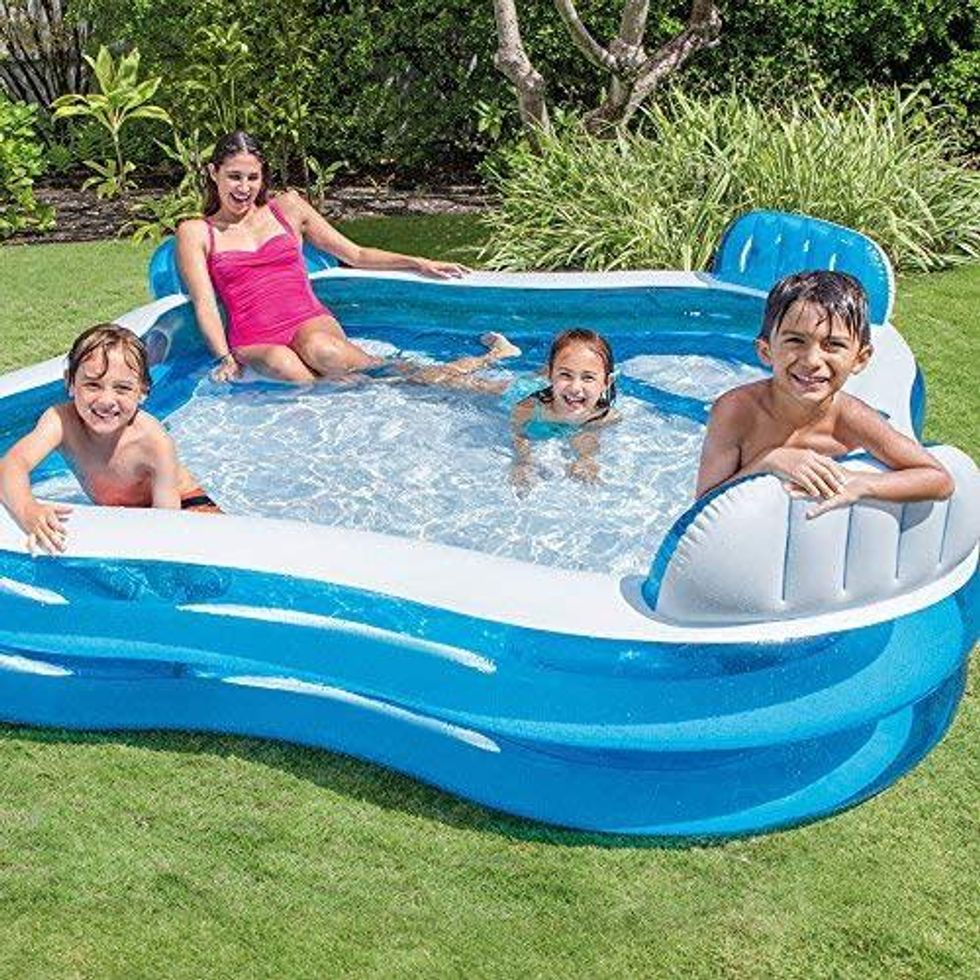 blue and white pool sitting in the backyard with a mom and three kids inside it