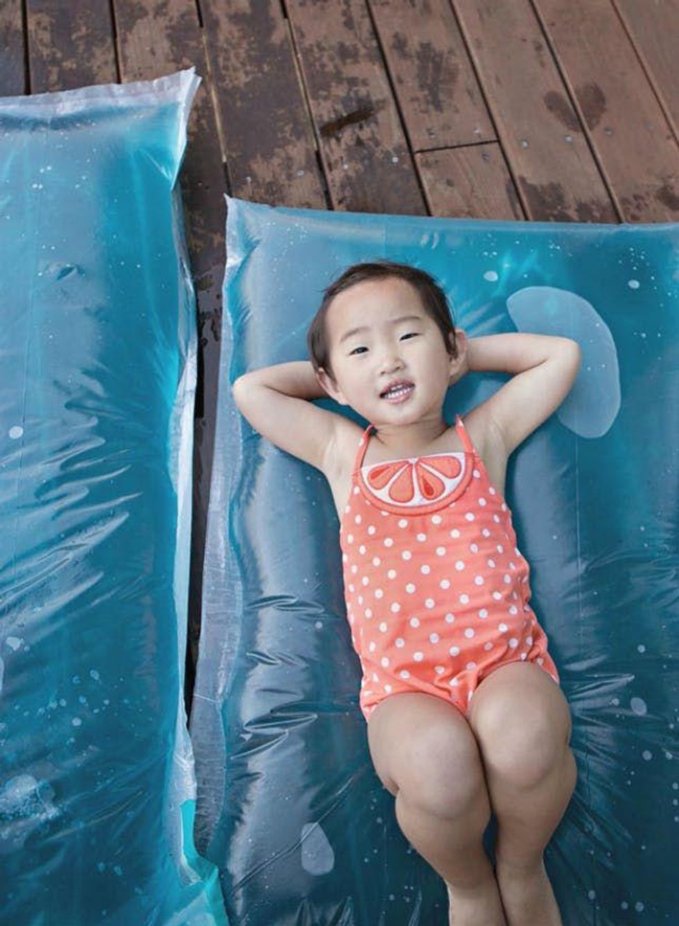 child lays on blue water blob in an orange polka dot swimsuit