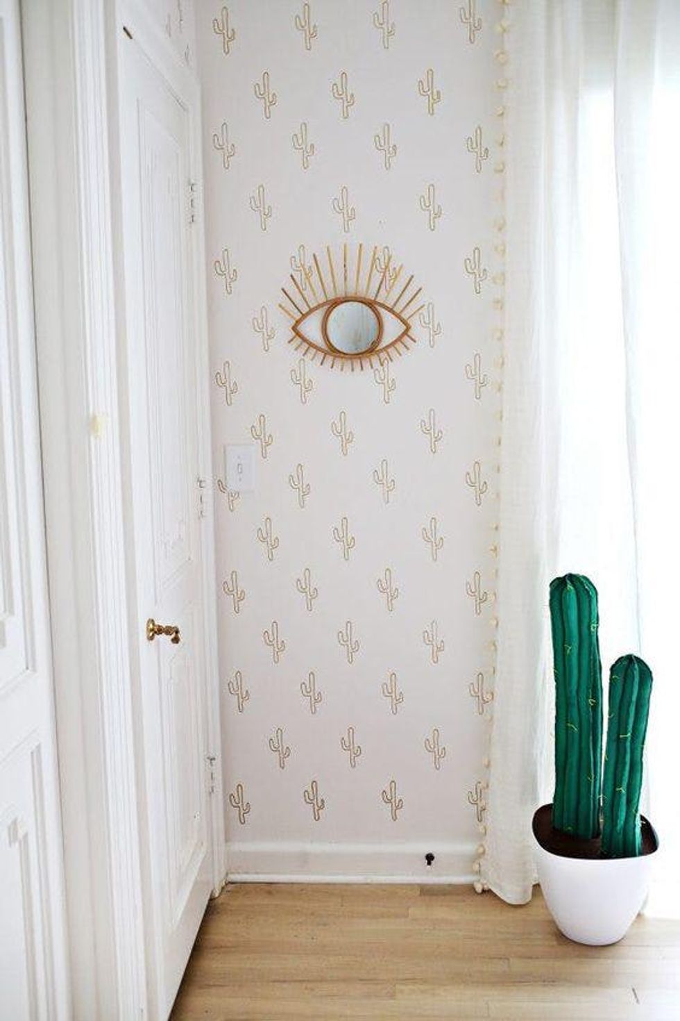 white wall paper with golden cacti and an eye mirror with a cactus plant on the ground