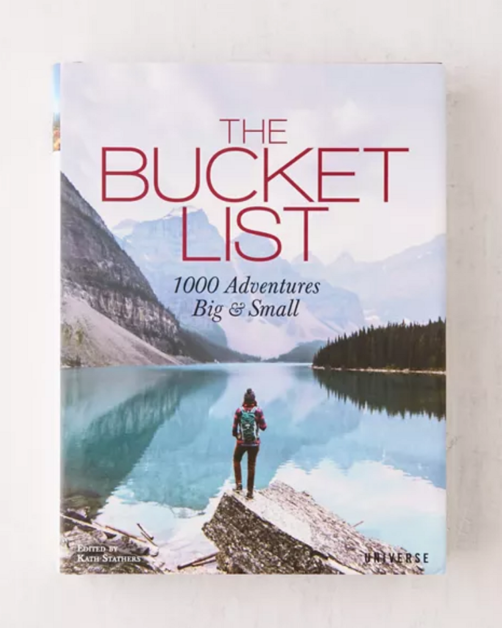 colorful bucket list book with woman standing on a rock looking at the water