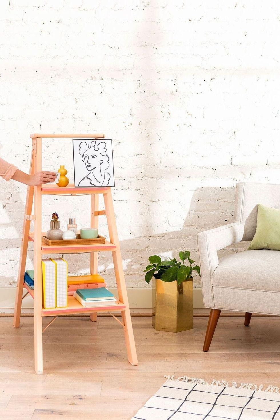 model sets a glass of wine on a diy shelf with decor in a living room beside a plant in a gold pot