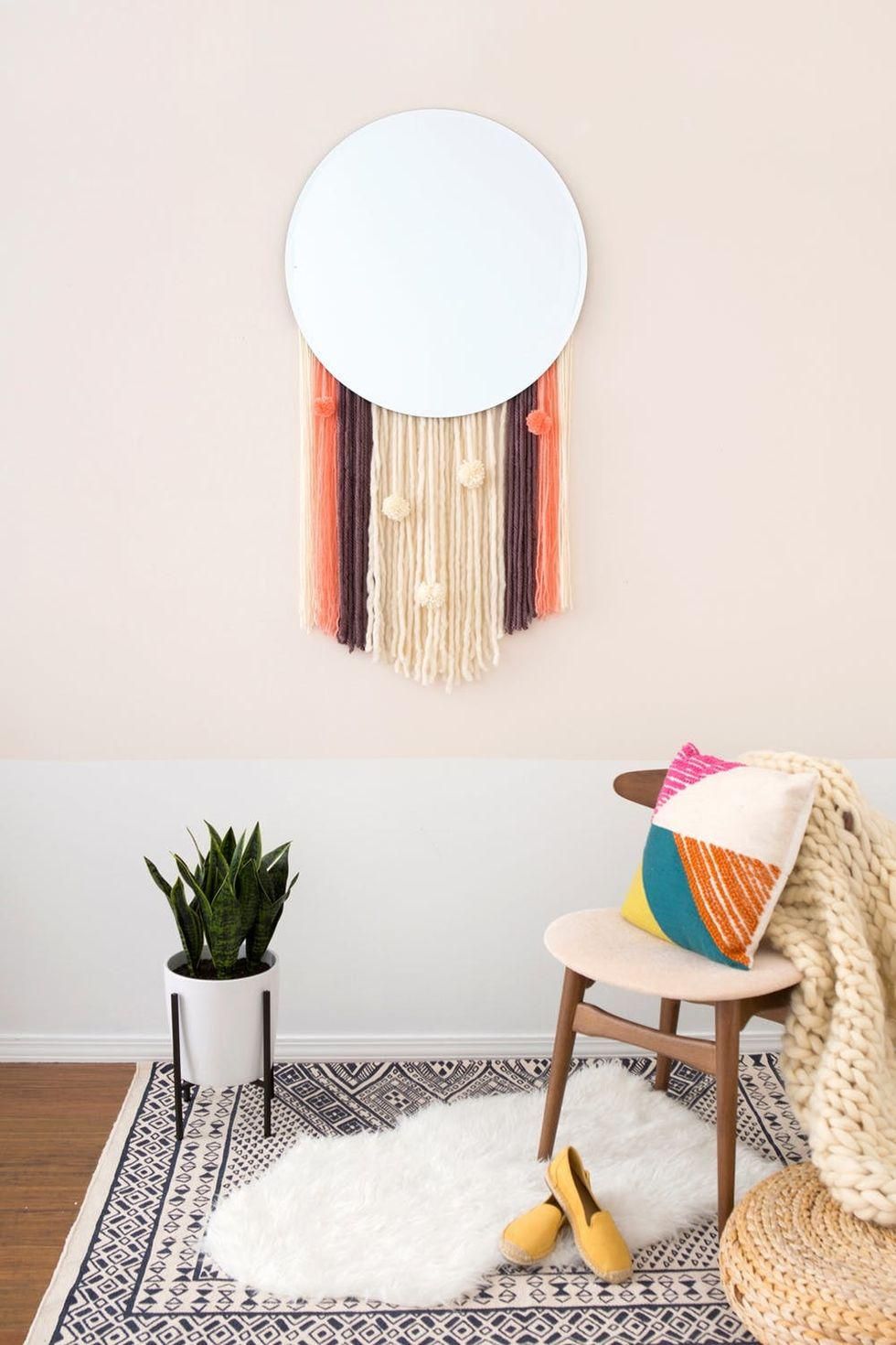 circular mirror with tassel detail on a pale wall over a plant stand, white fur rug, and circular chair