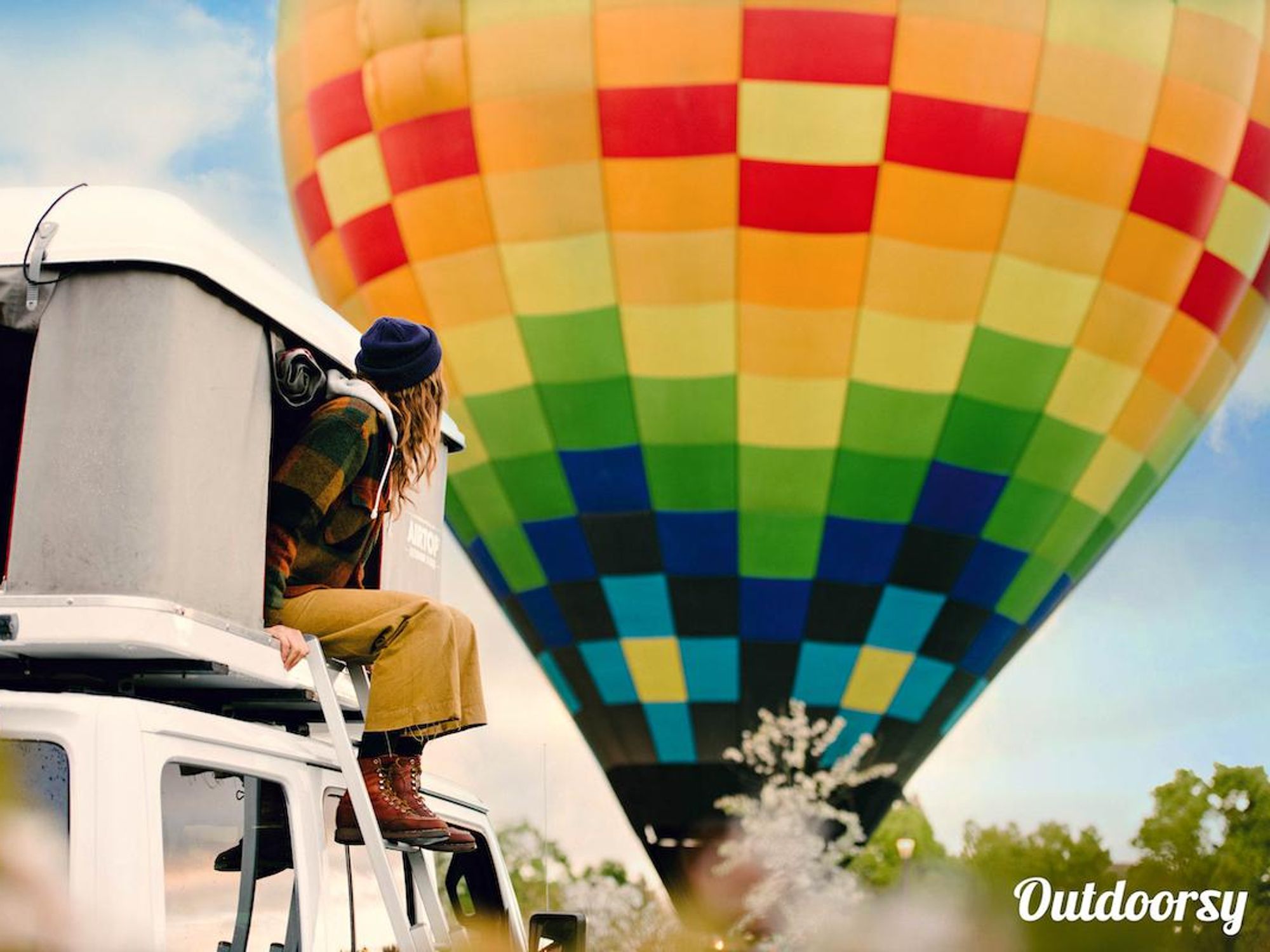 girl sits on a camper van looking at a hot air balloon