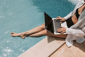 woman sitting poolside using laptop on summer break