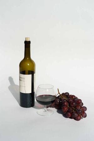 a glass of red wine with red grapes and a wine bottle