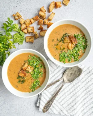 Vegan dill pickle soup is in a white bowl next to spoons. 