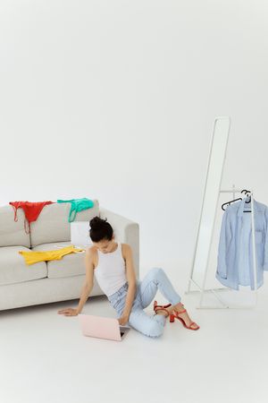 woman on her laptop with colorful clothes strewn on gray sofa