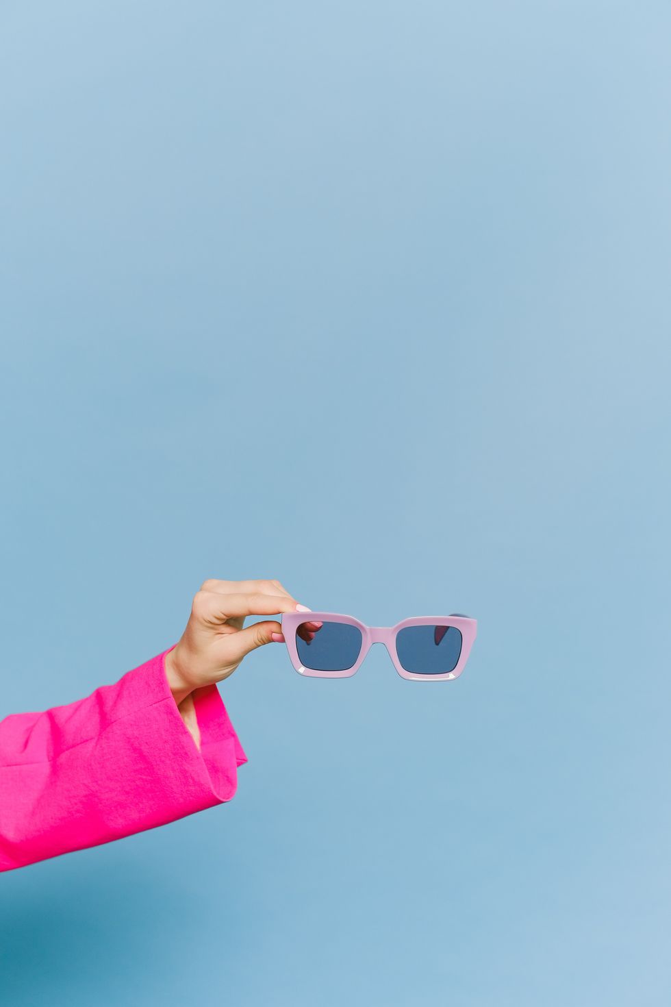 person holding pink sunglasses against a blue background