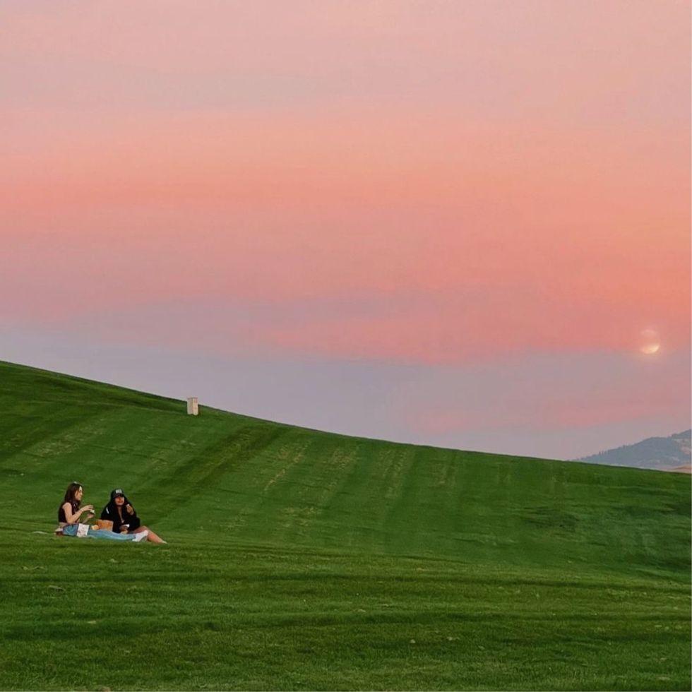 two girls having a picnic at sunset on a hill