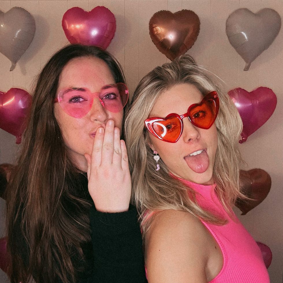 two girls in heart sunglasses posing in front of a wall of heart balloons