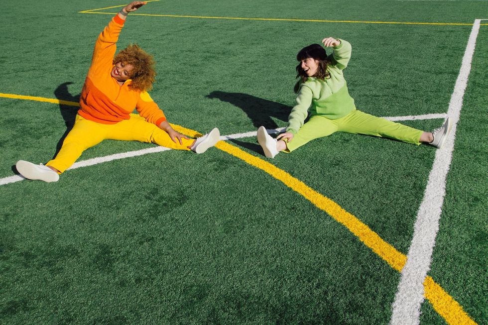 Two women stretching on a soccer field smiling working out