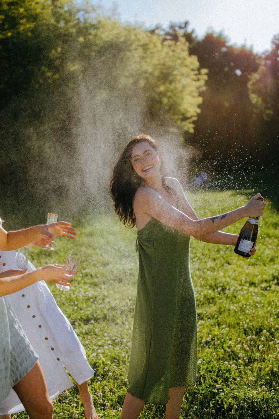 wedding guest in green dress pops champagne going to a wedding single