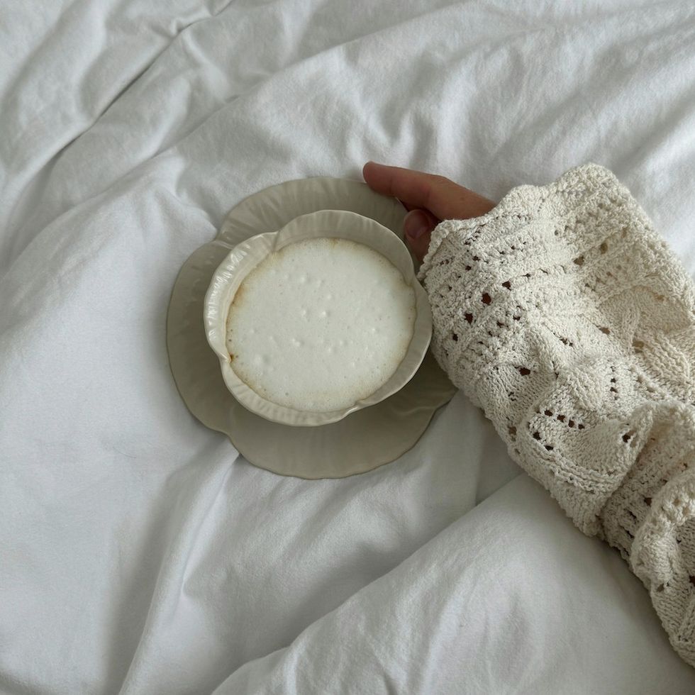 woman holding a cute coffee cup and saucer with a cappuccino in it in bed