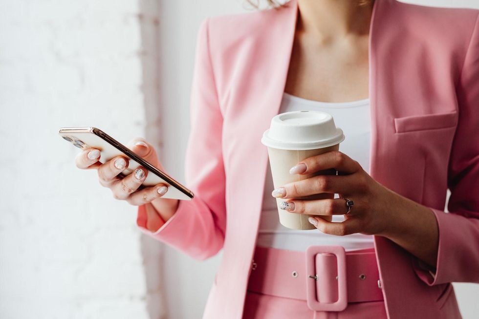 woman holding coffee and looking at phone