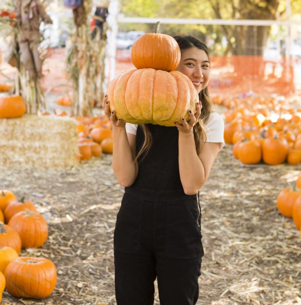 woman holding pumpkins while wearing a black jumpsuit Fall Vibes