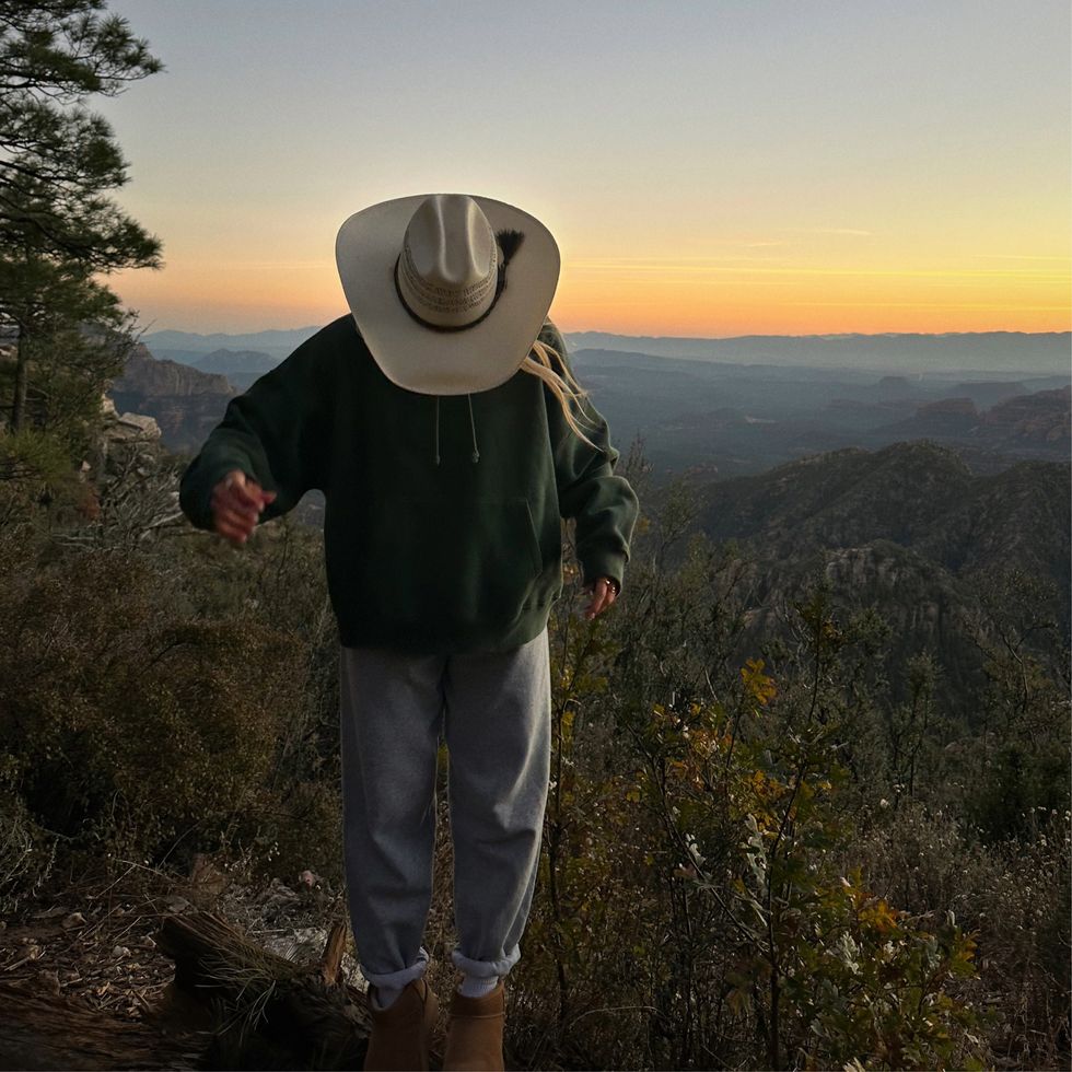 woman in a cowboy hat hiking in lush mountains at sunset