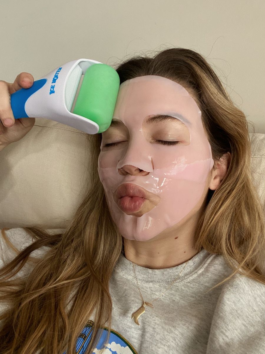 woman using an ice-roller on her sheet face mask