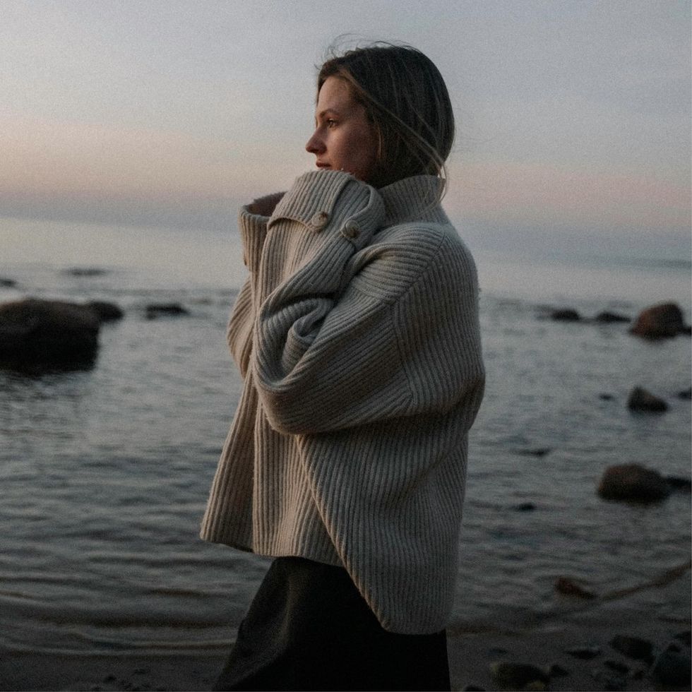 woman wearing a sweater staring out at the ocean at sunrise