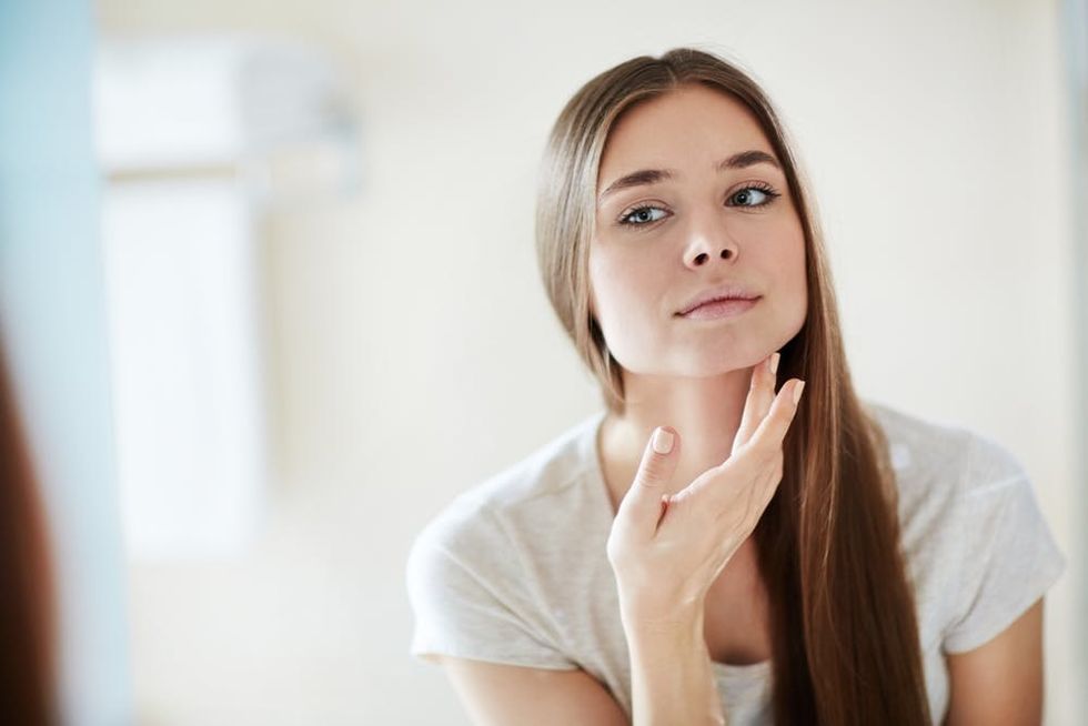 Young woman touching her face while looking in the mirror. 